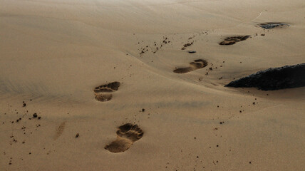 Pegadas humanas na areia dourada de uma praia tropical, sob o sol intenso e com o mar calmo ao fundo, simbolizando paz, viagem e momentos de tranquilidade