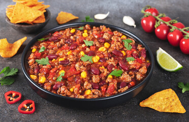 Meat mexican stew with beans, corn and tortilla chips chili con carne on gray background. Tex-Mex cuisine.