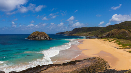 Fototapeta premium Praia paradisíaca em Fernando de Noronha, com mar turquesa, areia dourada e vegetação preservada. Cenário amplo que destaca a beleza natural e a tranquilidade do arquipélago brasileiro