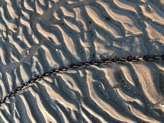 Textured beach sand with a metal chain tidal ripples texture background