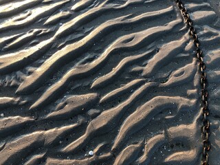 Textured beach sand with a metal chain tidal ripples texture background