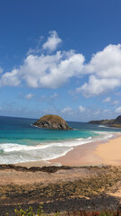 Praia do Leão com areia dourada, mar azul intenso e morros verdes ao fundo, revelando cenário...