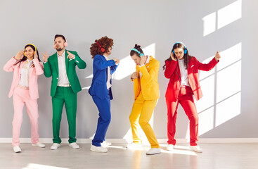 Happy playful people wearing bright vivid color suit dancing, funny disco, rock and roll lover active dancers, listening cool music in headphones with joy to enjoy party, overjoyed excited young group