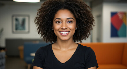 A beautiful young black woman with curly hair smiles confidently at the camera in a modern office setting