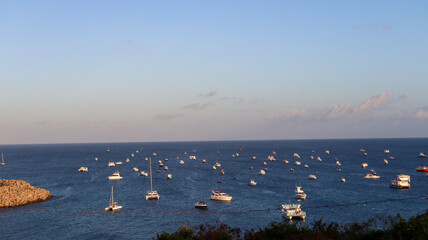Barcos coloridos ancorados na orla de Fernando de Noronha, com mar azul cristalino e o Morro do Pico ao fundo em um dia ensolarado