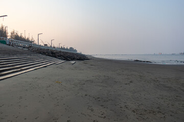 Gentle waves meeting rocky shore with ship fleet on horizon in Patenga, Bangladesh.