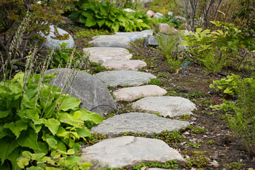 A tranquil garden path made of natural, irregular stepping stones surrounded by lush plants 