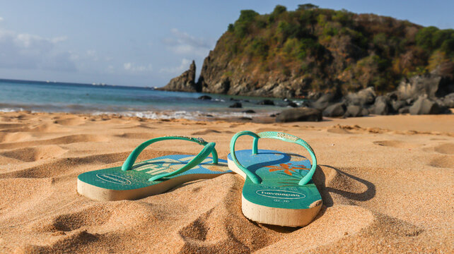 Chinelo Havaianas com tem&aacute;tica de Fernando de Noronha apoiado na areia da praia. S&iacute;mbolo cultural brasileiro em cen&aacute;rio paradis&iacute;aco com mar azul ao fundo. Noronha PE em 10 agosto 25