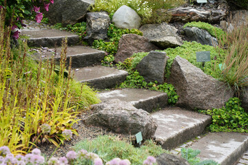 Rustic stone steps curve upwards through a lush rock garden with diverse foliage in Copenhagen,...