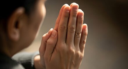 Person with hands clasped together in prayer or meditation in a softly lit and neutral toned environment