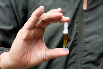 Man holding cannabis oil cartridge for vaping pen in hand