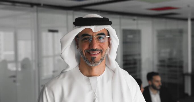 Head shot of happy middle-aged Arabic man, executive or Vice president dressed in traditional white thobe posing in boardroom, exuding confidence and authority, representing company, close up portrait