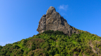 Morro do Pico em Noronha visto do litoral, destacando sua altura imponente, vegetação tropical e o mar cristalino ao redor