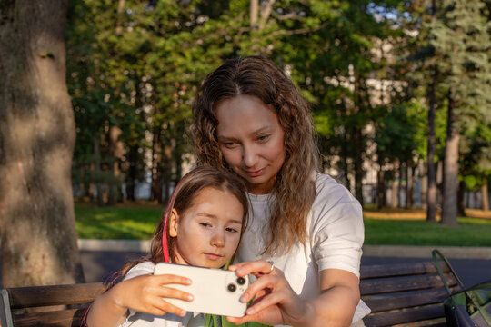 Mother and daughter taking selfie on park bench during sunny day