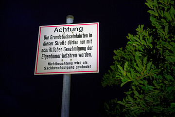German Achtung sign on metal pole with green leaves nearby