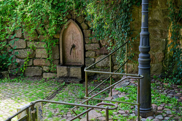 Stone wall fountain with arched frame and metal water spout trickling