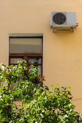 air conditioner on wall of an apartment building with view of green trees. ventilation and cooling of home or office during hot weather. installation maintenance of fan air conditioner. summer heat