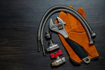 Adjustable wrench, ball valve with red handle, stainless steel tee fittings, leather safety gloves and rubber gaskets on wooden background, top view, copy space, closeup. Plumbing repair concept