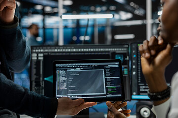 Close up of programmers coding on tablet in data center, refining algorithms for faster processing. IT workers using device in server room, conducting tests using software