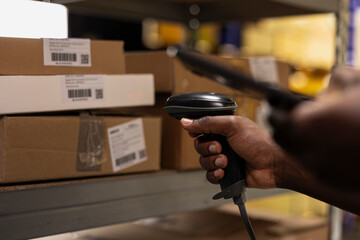 Black staff member using a barcode scanner to process shipping labels on boxes from industrial...