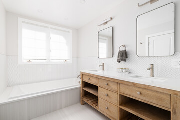 A bathroom with a natural wood cabinet with a white marble countertop and a white herringbone tile around the tub.