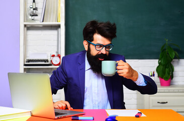 Surprised male teacher sitting at desk in classroom having coffee break. Exam in university or...