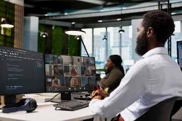 Tech company office coworkers working together via videocall, doing brainstorming on backup solutions to protect against data loss. African american man coding during online teleconference
