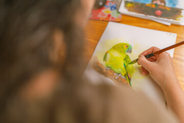 Graphic designer painting a parrot with watercolors in home studio