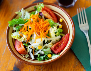 Plate contains portion of salad from fresh China cabbage, grated carrot, corn, tomato complemented by small glass of wine.