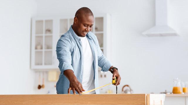 African american man assembly wooden furniture at home by yourself, woodwork and construction, Handyman at table with tools, measuring with tape desk in kitchen interior, empty space, panorama