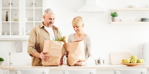 Chores, housekeeping, buying together at free time, couple unpacking fresh products from market in kitchen. Smiling adult male and female look in eco bags with groceries in modern interior, copy space