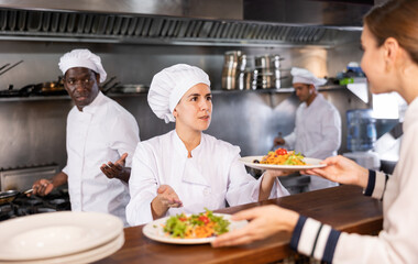 Female chef serving ready meals to visitors of restaurant