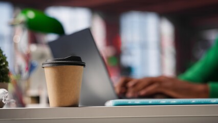 Male freelancer drinking coffee and solving his daily assignments at home, works on freelancing tasks. Black guy multitasking and answering emails, lifestyle from modern loft. Camera A.
