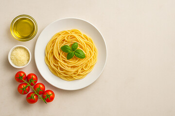 Plate of spaghetti with basil, tomatoes, olive oil, and parmesan on beige background