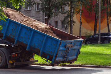 A blue dump truck unloads sand in a residential courtyard of high-rise buildings in Narva, Estonia....