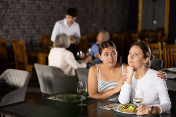Young woman comforting upset female friend during friendly meeting over dinner in restaurant