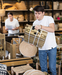 Focused young guy looking with interest at package of folded wooden chair for using in outdoor...