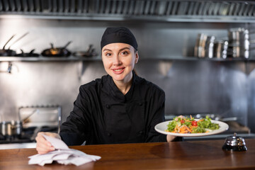 Portrait of confident woman chef working in modern open kitchen, checking orders and giving out ready salad
