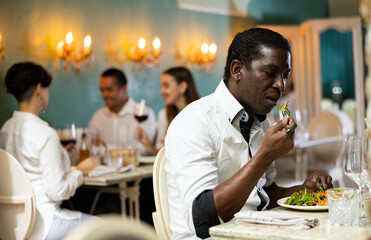 Single man eating salad at the restaurant with a group of young people on the background