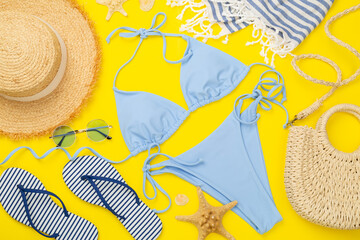 Blue bikini with beach accessories on color background, top view