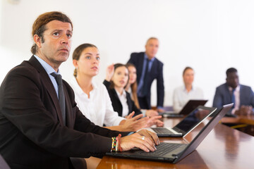 Fototapeta premium Businessman using laptop during conference in meeting room. Man sitting at desk with colleaugues.