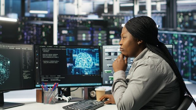 Data center technician using artificial intelligence deep learning models to configure hardware. African american woman works on AI programming language in server room, optimizing system, camera B