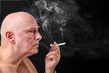 Obraz premium Middle aged man smoking a cigarette,as thick unhealthy smoke flows from his mouth,England,United Kingdom.