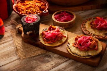 Panuchos, a typical dish from Yucatan, Mexico. A handmade, fried corn tortilla filled with beans, topped with cochinita pibil, pickled red onion, and habanero pepper.