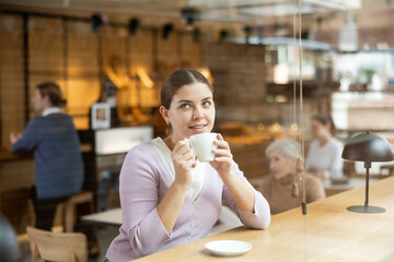 Relaxed woman sitting alone drinking coffee in quiet cafe