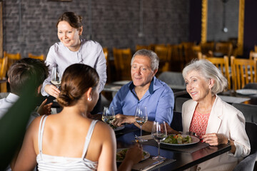 Cheerful elderly couple spending time with young friends in cozy restaurant. Man and woman having...