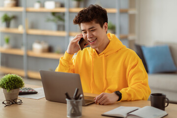 Mobile Communication. Smiling Asian Male Freelancer Talking On Cellphone And Working On Laptop At...