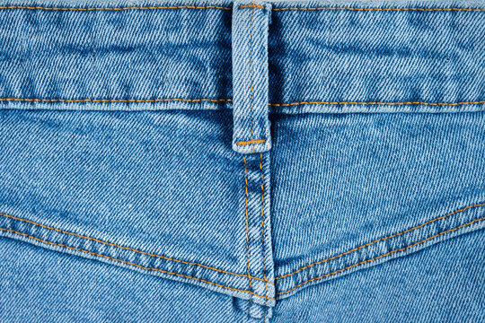 Detailed close up, macro of blue denim fabric with visible seam and belt loop, back side of jean pants. Textile texture background for fashion, clothing, fabric, and jeans design concepts.