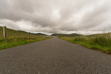 A road with a fence on the side and a cloudy sky in the background