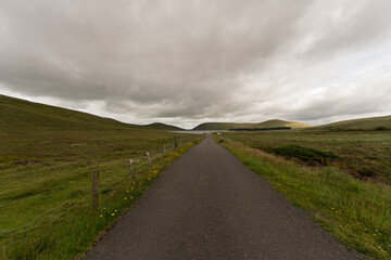 A long road with a fence on the side and a cloudy sky in the background